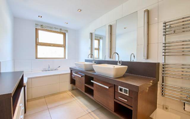 Bathroom with double sinks, a towel warmer, and a shower